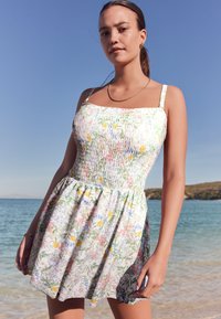 Mini abito floreale con corpetto arricciato, spalline sottili e gonna svasata. Presenta uno sfondo chiaro con motivi botanici colorati.