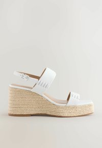 Witte wedge sandalen met een geweven jute plateau. Voorzien van een brede enkelband en een voorband met uitsparingen. Gladde afwerking en open teen ontwerp.