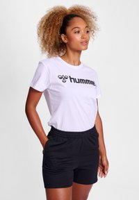 Hvid bomulds t-shirt med et sort "hummel" logo, parret med sorte shorts med elastisk talje og sidelommer.