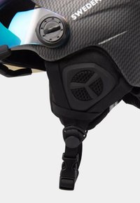 Sort carbonfiber-hjelm med en blå reflekterende visir, justerbar skive og sort rem. Har en struktureret sidepanel med ventilation.