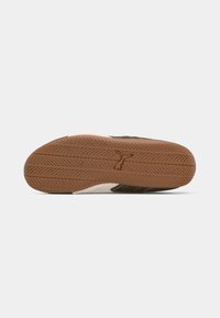 Suela de zapato informal con suela de goma texturizada marrón que presenta un logotipo central con forma de perro sobre un fondo blanco.