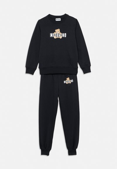 Completo felpa e pantaloni della tuta neri con orsetto e logo "MOSCHINO" stampati sul petto e sulla coscia.