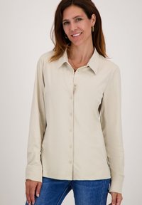 Beige overhemd met lange mouwen, een kraag, knopen aan de voorkant en een zachte textuur, gecombineerd met blauwe jeans.