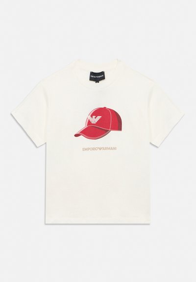 Camiseta blanca de manga corta con un gráfico de gorra de béisbol roja y el logo de Emporio Armani impreso debajo de la imagen de la gorra.