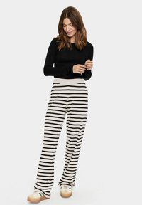 Pantalons larges rayés en tissu beige et noir, avec une taille confortable. Associés à un haut ajusté à manches longues noir et des baskets.