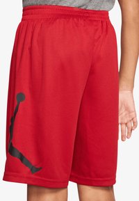 Pantalones cortos deportivos rojos hechos de una malla transpirable, con un logotipo de silueta negra en el costado, con una cinturilla elástica y un ajuste holgado.