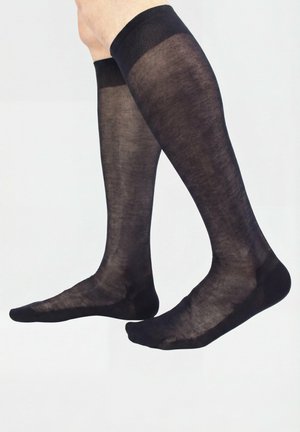 Legs wearing sheer black knee-high socks with reinforced toes and cuffs, shown against a plain white background.