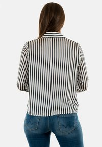Camicia a righe con linee verticali blu navale e bianche, dotata di colletto e maniche lunghe, abbinata a jeans blu a vita media con tasche.