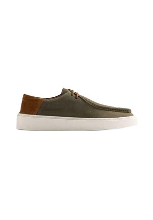Zapato casual de ante verde oliva de perfil bajo con parche marrón en el talón, cordones delanteros y suela de caucho blanca gruesa, vista lateral.