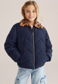 Chaqueta de plumas marina con un cuello de piel sintética de leopardo, textura de rombos y cremallera dorada. Combinada con unos pantalones cargo azul claro.
