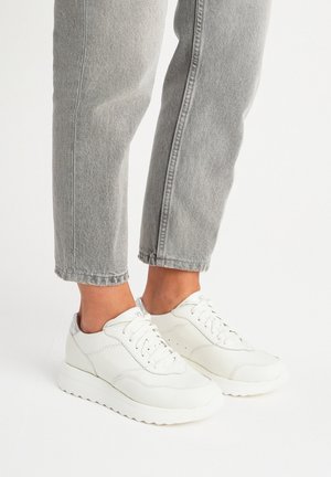 Białe skórzane trampki z teksturowanymi akcentami, zaokrąglonym palcem i sznurowaniem, w zestawieniu z szarymi, krótkimi dżinsami.