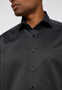 Zwarte overhemd met knopen, voorzien van een gestructureerd patroon, spitse kraag en een borstzak. Heeft zwarte knopen en een gladde stofafwerking.