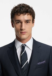 Dark navy suit with subtle checks, white dress shirt, striped tie, and patterned pocket square. Smooth texture with structured fit.