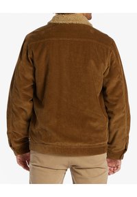 Ruskean corduroy takki, jossa on vaaleanruskea shearling-kaulus, vertikaalista ribbitekstuuria ja napilla varustetut hihansuut, esitettynä takaa.