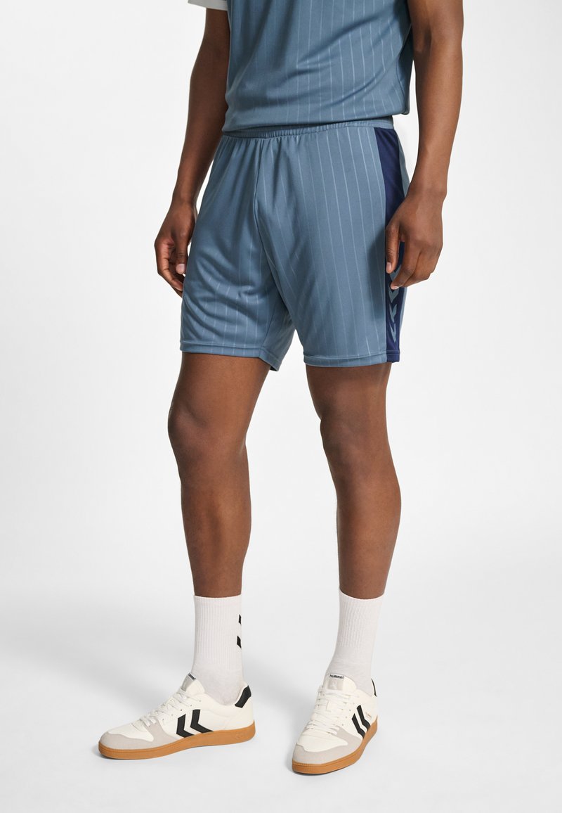 Ljusblå träningsshorts med mörkblå sidodetaljer, vertikala nålrandiga ränder, resårlinning och fuktavvisande tyg; matchas med vita sneakers.