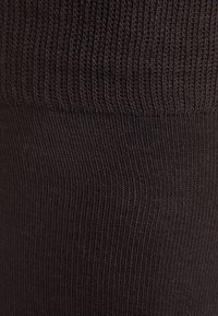 Calze nere a coste realizzate in un materiale elastico, con una texture fine e un motivo uniforme di linee verticali.