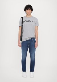 Grå bomull T-skjorte med svart tekst, kombinert med blå denimjeans og hvite sneakers. Har en skulderveske.