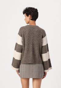 Pullover in tessuto a maglia color marrone con maniche a righe crema, orlo cropped e bordi a costine. Indossato sopra una gonna a quadri, che mette in risalto le texture contrastanti.