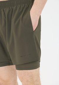 Dunkelolivgrüne Sportshorts mit elastischem Bund, Seitentaschen und Innenfutter. Mit "ENDURANCE"-Logo in der Nähe des Saums.