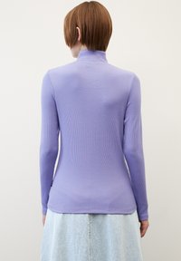 Haut à manches longues en maille côtelée lavande avec un col montant, forme ajustée et texture lisse, associé à une jupe en jean bleu clair.