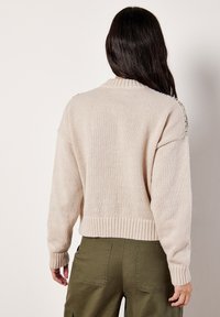 Beżowy sweter dzianinowy z prążkowanym wykończeniem u dołu i przy mankietach. Posiada okrągły dekolt i lekko oversize'owy krój. Wykonany z miękkiego, teksturowanego materiału.