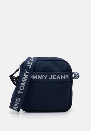 Bolso cruzado cuadrado en azul marino con cierre de cremallera, que presenta una correa con el logo impreso y una textura de tela duradera. Correa ajustable para mayor comodidad.