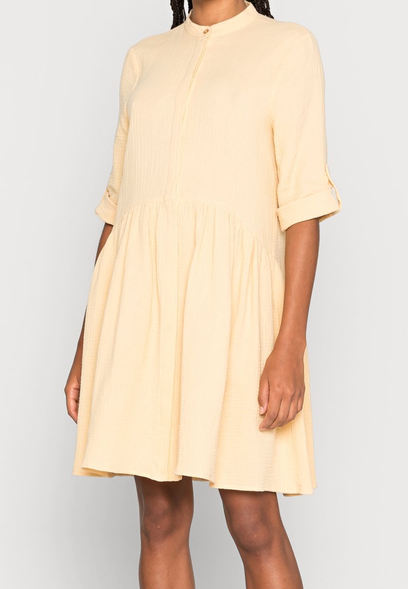 Yellow cotton dress with a buttoned collar, three-quarter sleeves, and gathered skirt. Textured fabric with a relaxed fit.