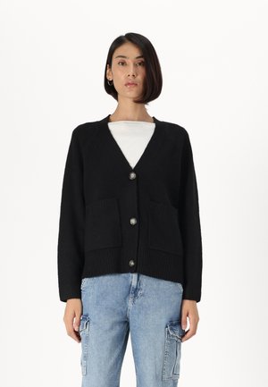 Svart cardigan med v-hals, som har to frontlommer og sølvknapper. Laget av et mykt, teksturert stoff, med løse ermer.