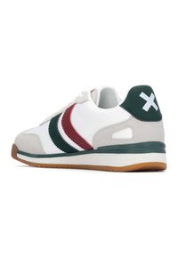 Zapatilla deportiva blanca con rayas verdes y marrones, hecha de materiales de ante y cuero liso, suela de goma y un acento trasero con un signo más blanco.