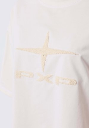 Crème-kleurig T-shirt met een textuur van een beige sterlogo en "PXP" in een vergelijkbaar materiaal, voorzien van een ronde halslijn en korte mouwen.