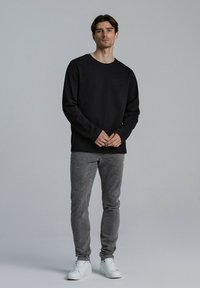 Czarny długi rękaw sweatshirt z okrągłym dekoltem, w zestawieniu z jasnoszarymi dżinsami i białymi trampkami. Prosty design, bez widocznych wzorów czy logo.