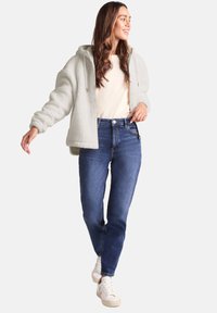 Light grey plush hoodie with a hood, paired with blue straight-leg jeans and white sneakers, creating a casual outfit.