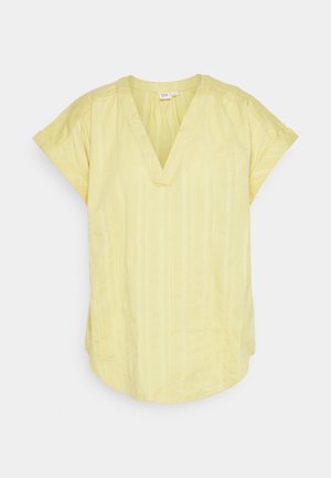 Blouse jaune pâle à manches courtes avec col en V, coupe ample et texture subtile à rayures verticales sur fond blanc.