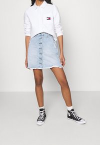 White long-sleeve collared shirt with a pocket logo, paired with a blue denim button-front skirt featuring frayed hem and distressed details.