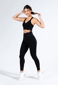 Czarny sportowy biustonosz i legginsy z wysokim stanem, oba wykonane z elastycznego materiału. Charakteryzują się skróconym krojem i dopasowanym kształtem, noszone z białymi trampkami.