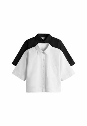 Młoda kobieta w ciemnej kurtce i pasiastym stroju kąpielowym stoi na tarasie z roślinnością i górami w tle, patrząc w bok.