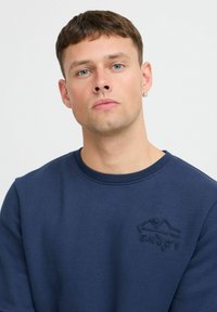 Felpa blu navy realizzata in tessuto morbido, con collo rotondo, polsini a coste e logo in rilievo "ENJOY" sul petto.