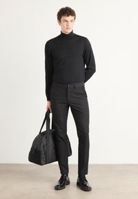 Melnā turtlenecka džemperis, melni pieguļoši bikses, spīdīgas melnas ādas kurpes un melna ceļojumu soma ar plecu siksnu. Minimalistiskais dizains.
