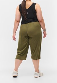 Svart ärmlös topp med olivgröna croppade byxor. Outfitten har en avslappnad passform och kompletteras av ljusa sneakers.