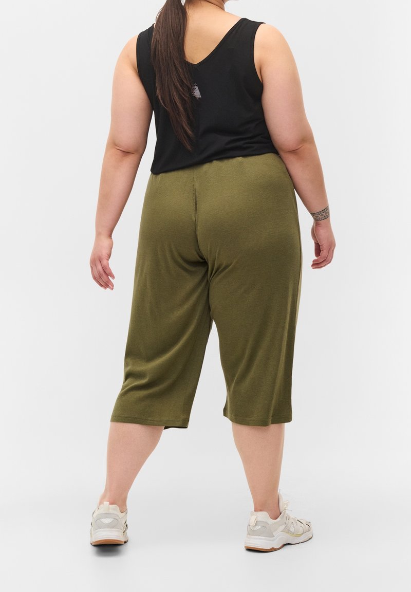 Svart ärmlös topp med olivgröna croppade byxor. Outfitten har en avslappnad passform och kompletteras av ljusa sneakers.