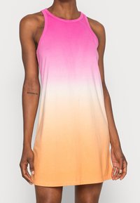 Abito casual senza maniche con una sfumatura di rosa, bianco e arancione indossato da una persona con tatuaggi sulle braccia su uno sfondo semplice.