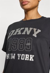 Μαύρο βαμβακερό κοντομάνικο μπλουζάκι με κοντά μανίκια, με έντονη ασημί επιγραφή: "DKNY 1989 SPORT NEW YORK." Λαιμόκοψη τύπου crew και άνετη εφαρμογή.