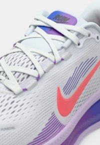 Scarpe da corsa in rete bianche con accenti rosa e viola. Presentano un'imbottitura spessa e motivi testurizzati sulla tomaia e sulla suola. I lacci sono bianchi.