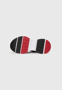 Sola de sapato com seções em preto, vermelho e branco. Apresenta borracha texturizada com padrões quadrados e um logótipo ao centro.