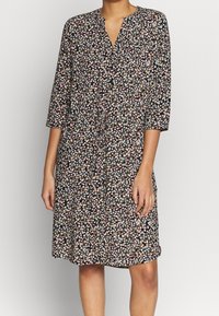 Blommig klänning i svart med trekvartsärmar. Har en V-ringning, åtsittande midja och en flödande kjol med ett livfullt flerfärgat blommönster.