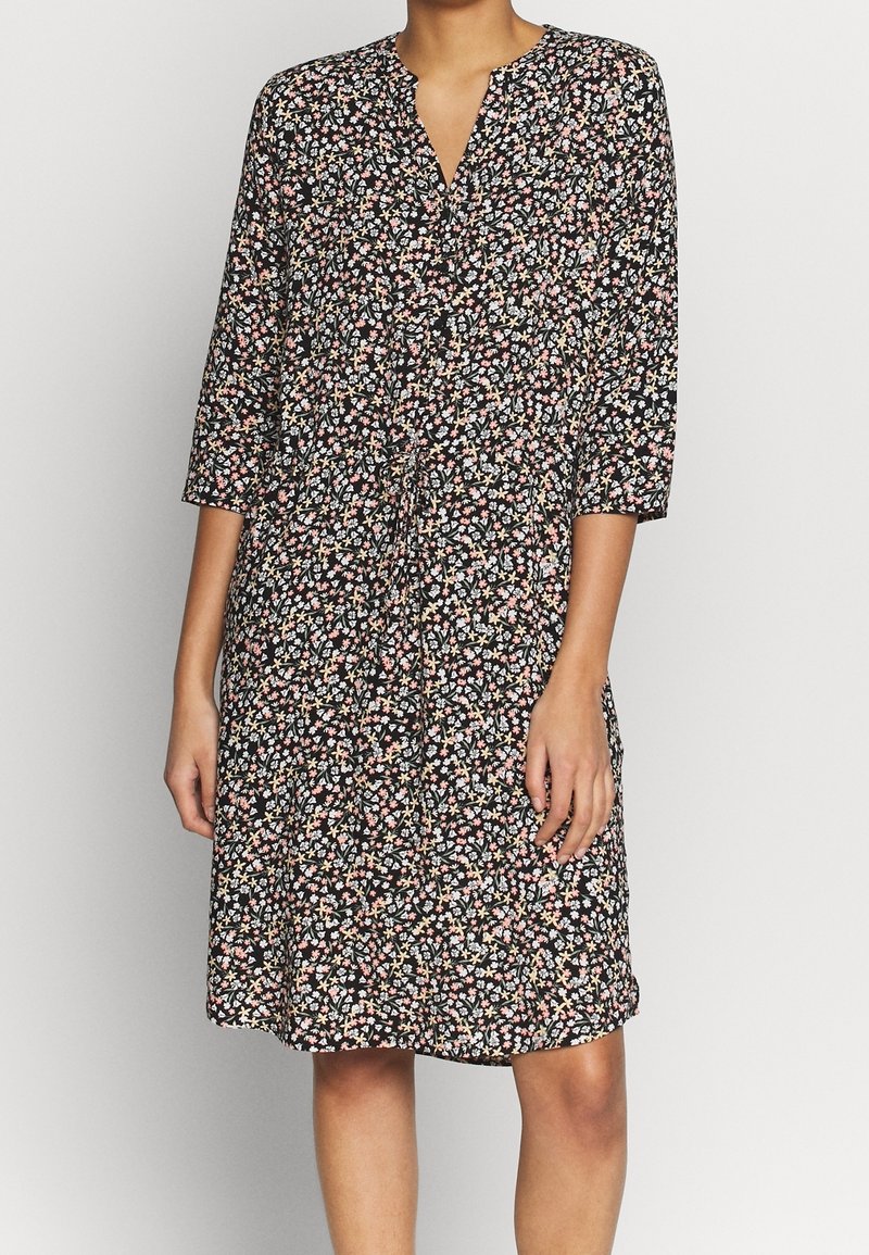 Blommig klänning i svart med trekvartsärmar. Har en V-ringning, åtsittande midja och en flödande kjol med ett livfullt flerfärgat blommönster.