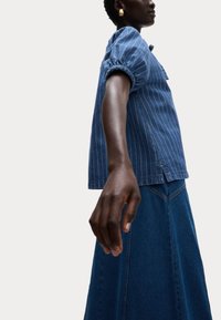 Top in denim con strisce bianche verticali, maniche a sbuffo e taschino sul petto, abbinato a una gonna in denim scuro con silhouette svasata.