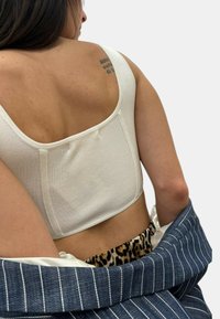 Top corto bianco a coste con scollatura quadrata, presentato su una giacca di jeans con strisce bianche e una cintura con stampa leopardo.