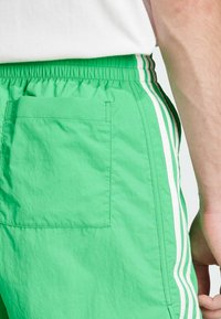 Πράσινα σορτς από ελαφρύ ύφασμα, με πίσω τσέπη, ελαστική μέση και λευκές κατακόρυφες ρίγες κατά μήκος των πλευρών.