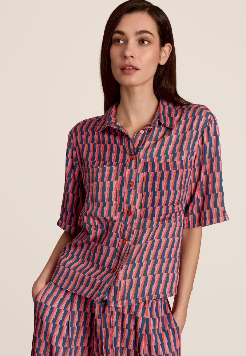 Kortebloesjes overhemd met knopen in marineblauw, rood en roze geometrisch patroon. Lichtgewicht stof, spread collar en één borstzak.
